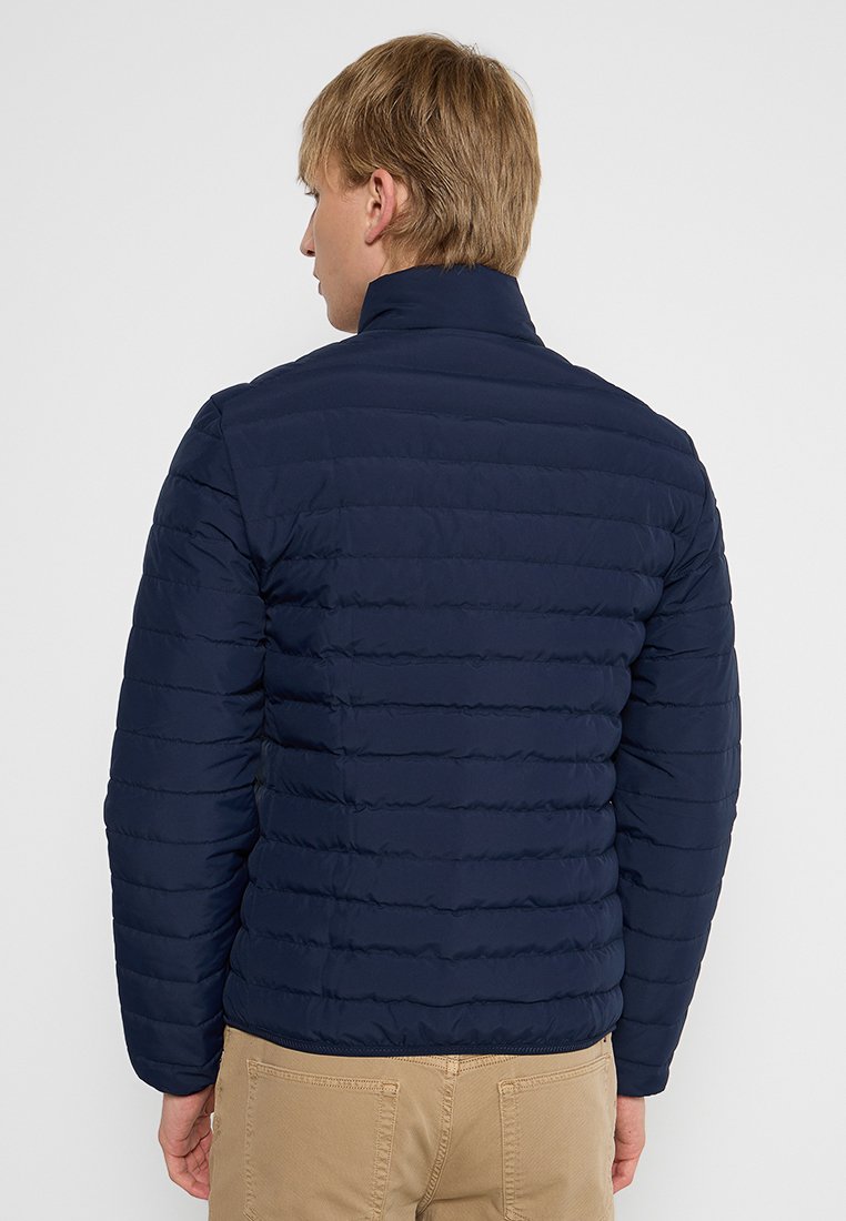 Veste rembourrée bleu marine avec un design matelassé horizontal, col montant et texture lisse, adaptée aux temps frais.