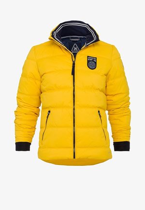 Doudoune jaune à texture matelassée, doublure de capuche bleu marine et écusson sur la poitrine. Dispose de poches latérales zippées et de poignets noirs.