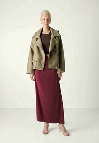 Olīvzaļš mākslīgās ādas motociklistu jaciņa ar sudraba detaļām, kas valkāta virs brūna topa un bordo maxi svārkiem. Caursūkņoti zābaki pabeidz izskatu.