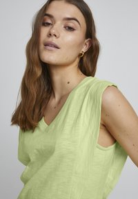 Top senza maniche verde chiaro con scollatura a V realizzato in un tessuto morbido, caratterizzato da una vestibilità rilassata e una trama sottile.