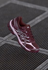 Maroon athletic shoe with mesh upper, white and pink accents, round toe, lace-up design, and textured sole.