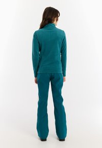 Teal fleece top met een hoge kraag, gecombineerd met teal broek. Beide hebben een gladde textuur en een getailleerd ontwerp voor actief gebruik.