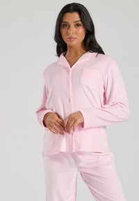 Lyserød pyjamas sæt med en knap-ophængt skjorte med lomme og lange ærmer, parret med matchende bukser. Blødt stof og løs pasform.