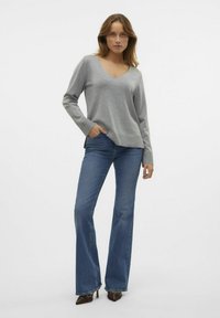 Pull gris à col en V avec des manches longues, associé à un jean bleu évasé. Le jean présente un design classique et une légère décoloration, complété par des talons bruns pointus.