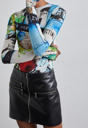 Person trägt ein farbenfrohes abstraktes Langarm-Top und einen schwarzen Leder-Minirock mit drei Reißverschlusstaschen vorne.