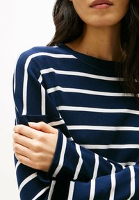 Maglietta a maniche lunghe blu navy con strisce orizzontali bianche, scollatura rotonda e tessuto morbido. Presenta maniche leggermente oversize.