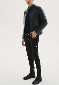 Černá kožená bunda se zipy, černé úzké kalhoty typu cargo s několika klopami kapes a zapínáním na druky, doplněné černými šněrovacími botami.