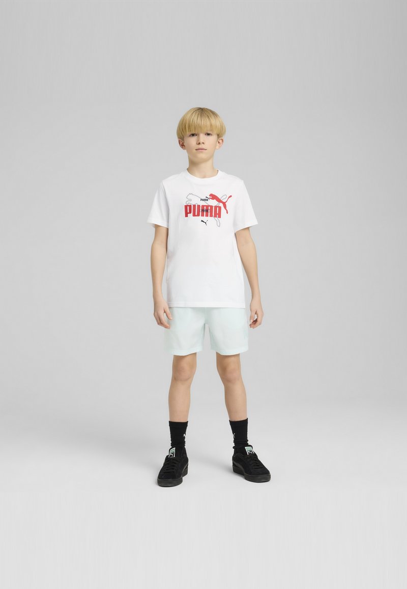 Bela bomba majica iz bombažne tkanine z rdečim logotipom "PUMA", v kombinaciji s svetlo metino kratkimi hlačami. Črne nogavice in črne športne čevlje dopolnjujejo videz.