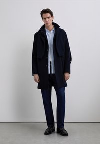 Tmavomodrý vlněný kabát s vysokým límcem, tmavě modré džíny a černé kožené boty. Košile je světle modrá s knoflíky. Obsahuje svetr přehozený přes kabát.