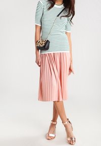 Pruhované mintové a bílé tričko s krátkým rukávem spojené s plisovanou růžovou midi sukní. Kombinováno s metalickými podpatky a malou kabelkou přes rameno se zvířecím potiskem.