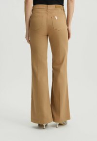 Uitlopende, high-waisted broek van tan stof. Bevat twee achterzakken en een zichtbaar logo label. Soepele textuur en op maat gemaakte snit.