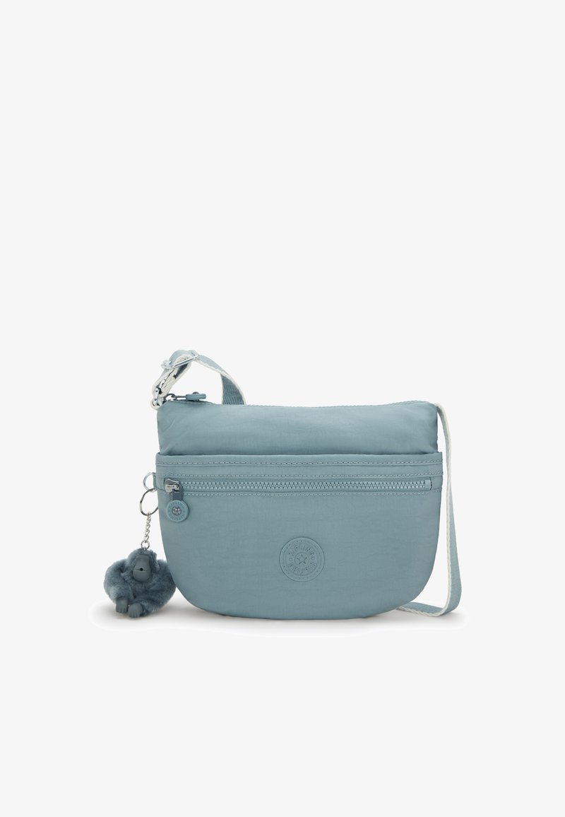 Crossbody taske i lyseblåt stof med en struktureret overflade. Har en lynlåslomme foran og en pelsagtig abe charmer. Justerbar skulderrem.