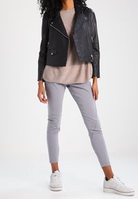 Veste de motard en cuir noir portée sur un pull beige clair, associée à un pantalon gris ajusté et des baskets blanches, offrant un look décontracté et moderne.