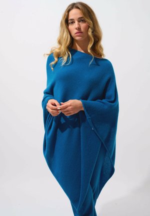 Sininen villa poncho, jossa on valuvampaa muotoilua, leveät hihat ja lentävä siluetti. Pehmeä rakenne, jossa on vain vähän ompeluyksityiskohtia.