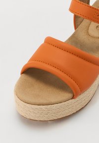 Oransje skinn kilehæl sandal med en bred, glatt sele. Har en teksturert kork-lignende såle og en semsket innersåle. Uthevet sømdetalj.