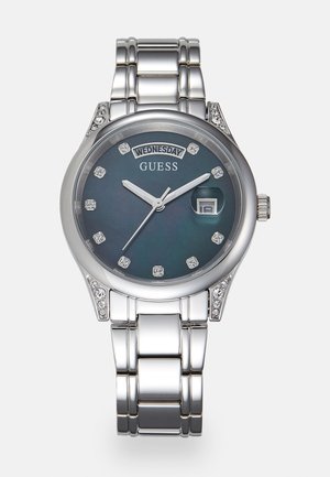 Silberne Metallarmbanduhr mit blauem Zifferblatt, Kristall-Stundenmarkierungen, Tages- und Datumsanzeige sowie dekorativen Kristallen an den Gehäuseanstößen und Gliedern des Armbands.