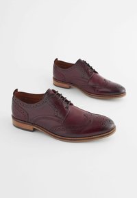 Chaussures habillées en cuir bordeaux avec des détails en brogue, à lacets et avec une semelle en cuir marron. Texture lisse avec des perforations décoratives.