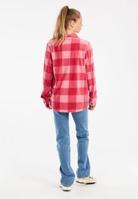 Camicia in flanella a quadri rossi e rosa con maniche lunghe, orlo arrotondato e polsini con bottone, abbinata a jeans blu chiaro e sneakers.
