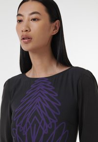 Vêtement noir avec un col rond et des manches longues, orné d'un grand motif abstrait violet. Tissu lisse avec une texture subtile.