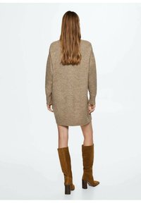 Robe pull en tricot beige avec une coupe décontractée, des manches longues et un ourlet côtelé, associée à des bottes en daim marron jusqu'au genou sur un fond neutre.