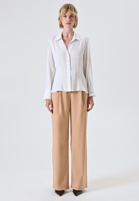 Witte lange mouw knoopshirt met een ontspannen fit, gecombineerd met lichtbeige wijde broek en puntige bruine hakken. Glad stofgevoel.