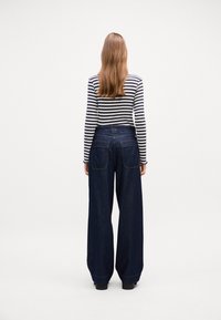 Bredde-lår mørkeblå jeans med høy midje og to baklommer, kombinert med en svart og hvit stripete langermet topp.