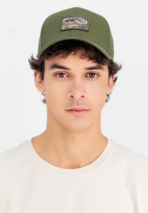 Olivgrüne Mütze mit strukturiertem Design und texturiertem Stoff, ausgestattet mit einem Patch mit Text und einem Camouflage-Muster auf der Vorderseite.