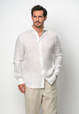 White linen button-up shirt with a collar, long sleeves, and a slightly relaxed fit. Features subtle texture and a curved hemline.