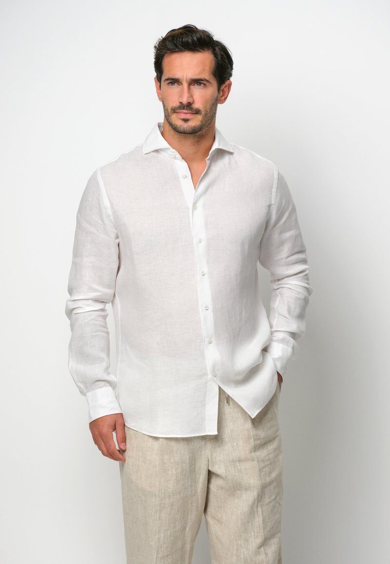 Camisa de lino blanca de botones con cuello, mangas largas y un corte ligeramente holgado. Presenta una textura sutil y un dobladillo curvado.