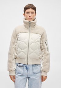 Világos bézs dzseki steppelt mintával és birka bundás részletekkel. Magas gallér, cipzáras zárás, bordázott mandzsetta és oldalsó zseb teszi teljessé a megjelenést.