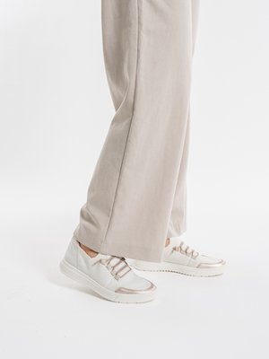 Person wearing beige wide-leg pants and white casual sneakers with beige accents, standing on a white floor against a plain background.