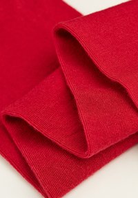 Rødt strikket stof med en glat tekstur, der har foldede kanter, som skaber bløde cylindrisk former.