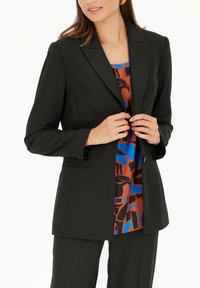 Czarna żakiet stylizowany na miarę, zapinany na pojedynczy guzik, z szpiczastymi klapami i długimi rękawami. Wewnątrz znajduje się kolorowy, abstrakcyjny wzór w odcieniach niebieskiego i brązowego.