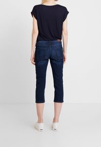 Tmavě modré zkrácené džíny vyrobené z denimu, s přiléhavým střihem, zadními kapsami a hnědou koženou nášivkou na pasu.