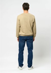 Beige sweatshirt met lange mouwen en blauwe jeans, met een relaxed fit. Witte sneakers met subtiele kleurnuances maken de outfit compleet.