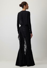 Sieviete stāv profilā melnā kleitā ar garām piedurknēm, kurai ir mežģīņu asimetriska uzmava, un matiem sakārtotiem bunā ar karājamiem auskariem.