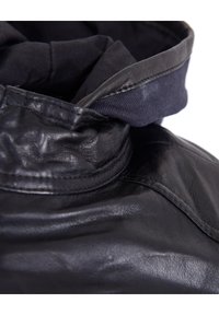 Schwarze Lederjacke mit hohem Kragen; zeichnet sich durch eine glatte, leicht zerknitterte Textur aus. Der Kragen hat ein kontrastierendes Detail aus Marineblau.