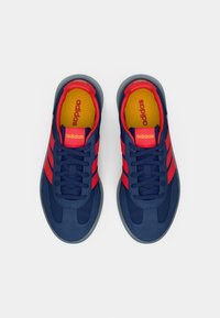 Mjeden plave atletske cipele s crvenim prugama, gornji dio od teksturiranog materijala, okrugli vrh i sivi gumeni potplat. Sadrži logotipe na jeziku i ulošku.