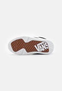 Die Sohle des Vans-Schuhs besteht aus einer weißen Zwischensohle, einer braunen Gummisohle mit einem Rautenmuster und einem auffälligen weißen Logo.