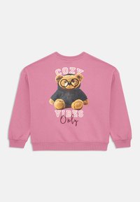 Sweatshirt rosa com um gráfico de um urso de óculos e capuz, texto a dizer "Apenas VIBRAÇÕES CONFORTE", e punhos e bainha canelados.