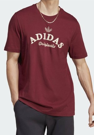 Bordeaux bomuld t-shirt med "ADIDAS Originals" i beige bogstaver, rund halsudskæring og korte ærmer, kombineret med mørke bukser.