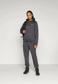 Quiltet mørkegrå hoodie med snøre i hætten, parret med grå bukser og sorte vandrestøvler. Har et logo på brystet.