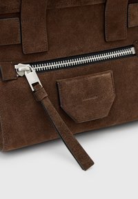 Borsa a tracolla in suede marrone con chiusura zip metallica, una piccola tasca frontale e dettagli neri a contrasto sui bordi e sulla tracolla.