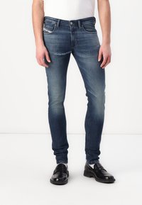 Slim-fit mörk denimjeans med diskret blekning och slitna detaljer. Har standard femficksdesign och metallknappstängning.