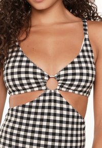 Top bikini a scacchi bianco e nero con design cut-out, dettaglio anello in metallo argentato al centro e spalline regolabili.