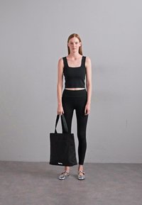 Top cropped nero e leggings abbinati a una borsa a tote nera. Ballerine argento con una finitura liscia. Design semplice con una silhouette elegante.