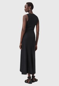 Abito maxi nero a coste con corpino aderente e gonna svasata, caratterizzato da uno scollo a barca e un design minimalista. Indossato con sandali neri.