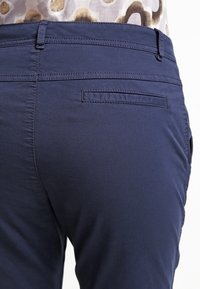 Marinblå byxor med bakficka, slät textur och rak design. Synlig sömnad längs midjebandet och fickkanterna.