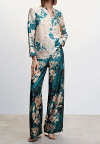 Floraler Satinanzug in Türkis und Creme, bestehend aus einer langärmeligen Bluse mit V-Ausschnitt und weit geschnittenen Hosen, die mit großen Blumenmustern verziert sind.