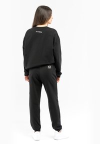 Black oversized sweatshirt and joggers made of soft fabric. Notable logo accents: "ICE ICEBERG" on the back and front of the pants.